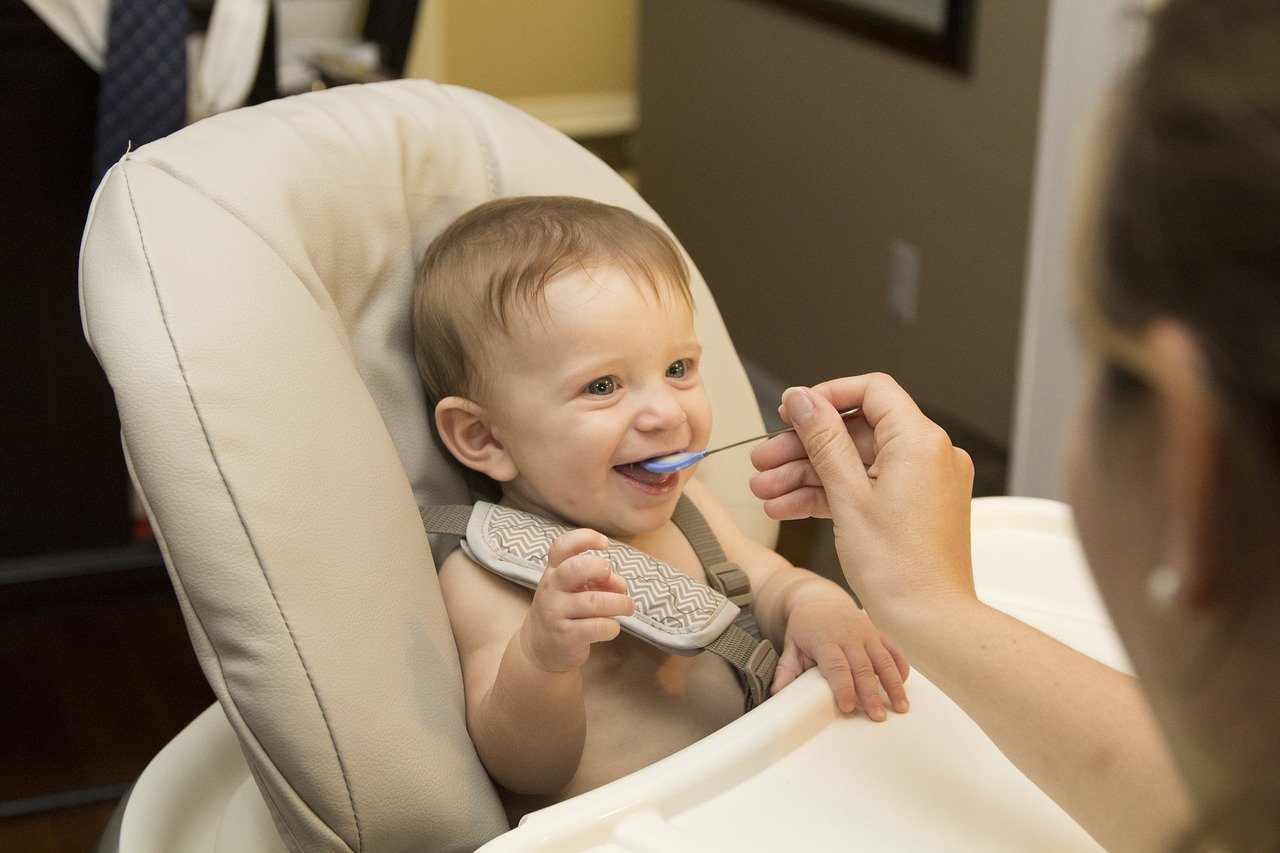 bébé souriant à qui une femme donne à manger à la petite cuillère