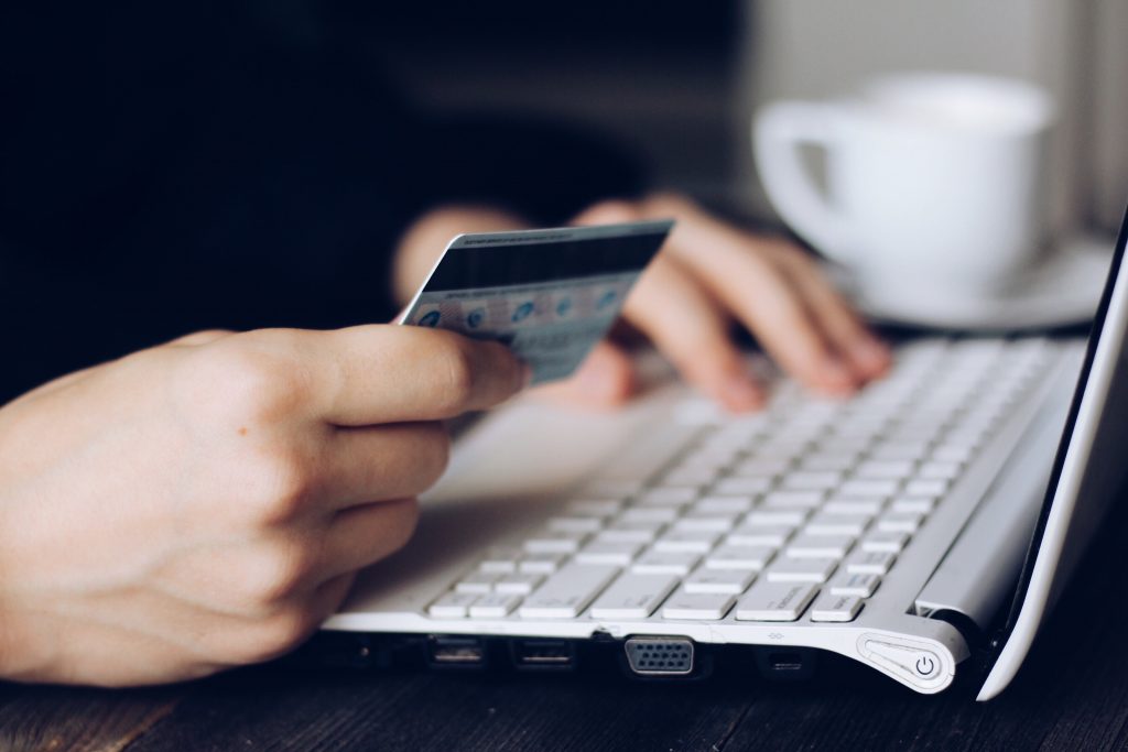 zoom sur les mains d'une personne qui tient une carte bancaire dans une main et tape sur un clavier d'ordinateur de l'autre