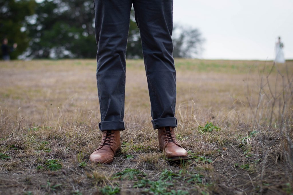 jambes d'un homme portant un chino foncé et des bottines à lacets marron