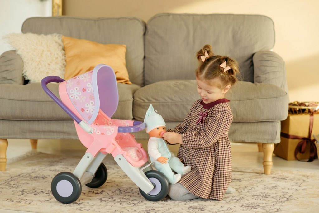 petite fille qui joue avec sa poupée et une poussette pour poupon dans le salon