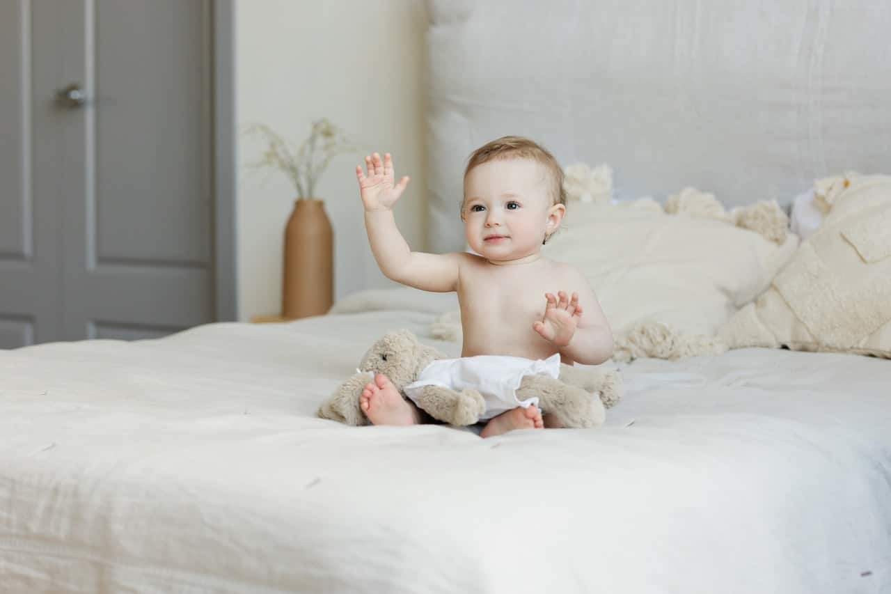 nouveau né assis sur un lit avec son doudou de naissance sur les genoux